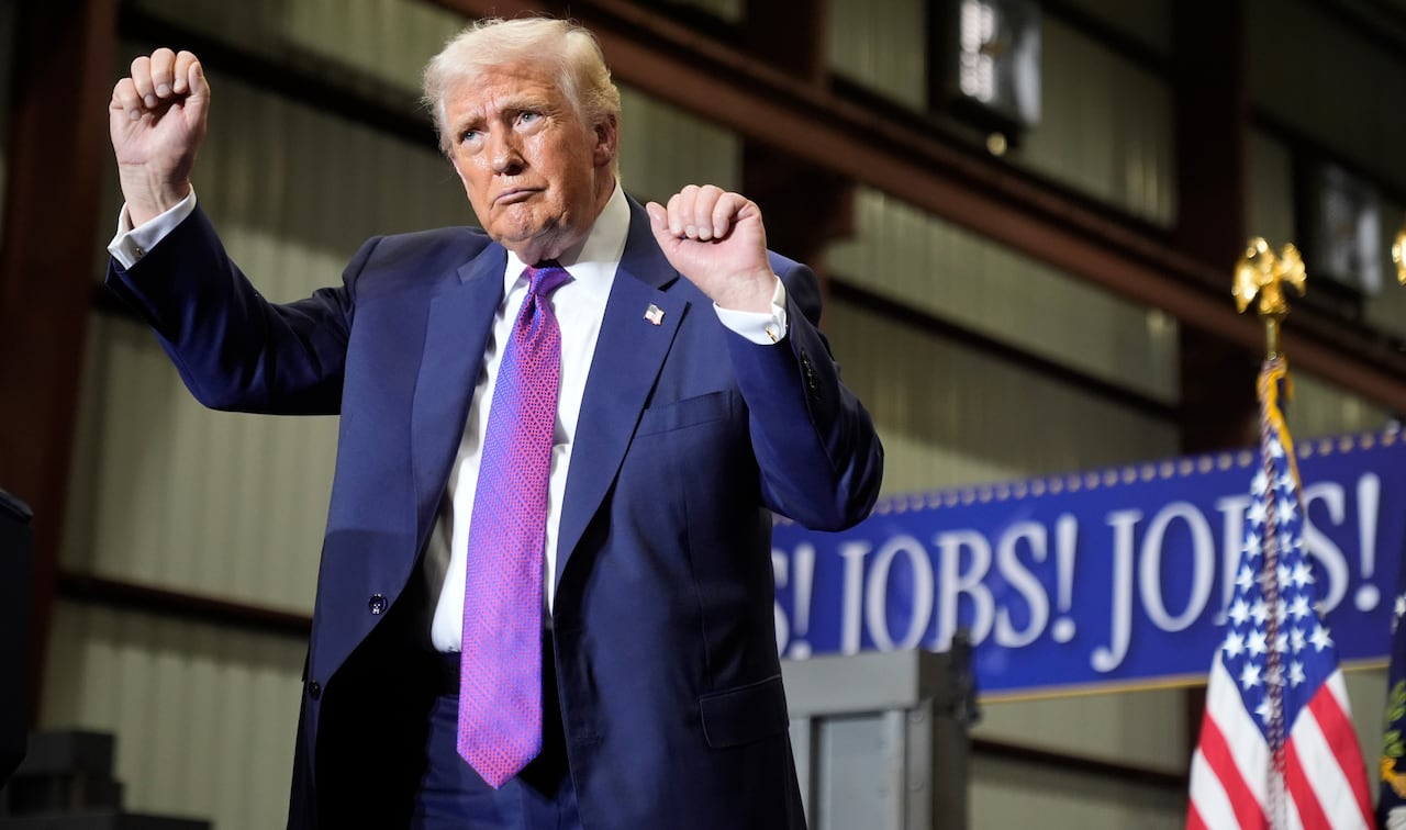Donald Trump holds his hands in the air while dancing in front of a U.S. flag and a sign that says 'Jobs! Jobs! Jobs!'