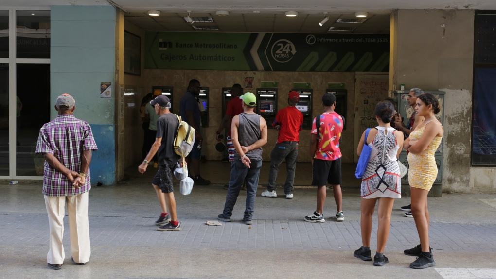 People stand in line outside a bank hoping to withdraw Cuban pesos from an ATM, in Havana, Cuba, Monday, April 22, 2024. (AP Photo/Ariel Ley)