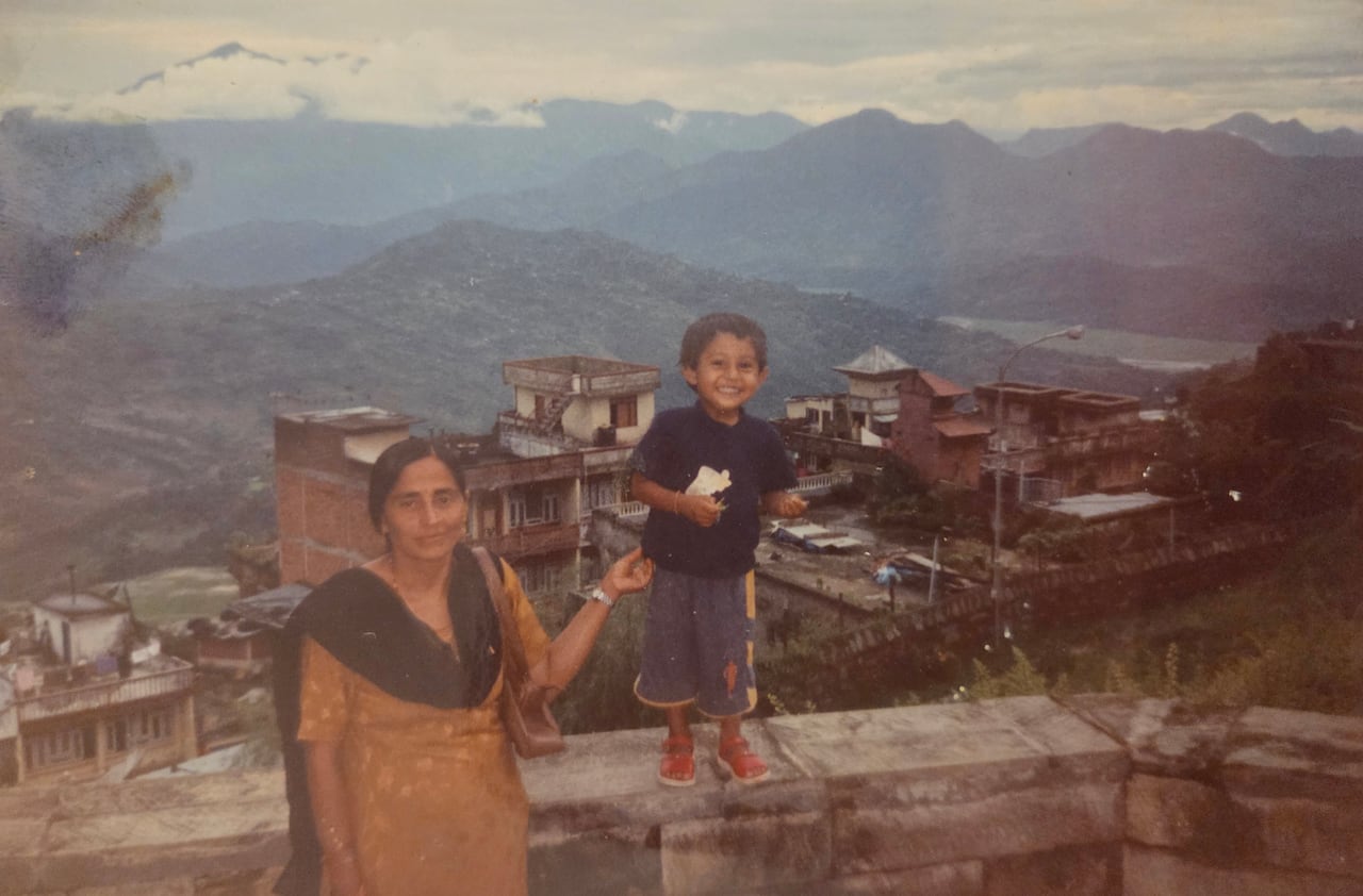 A photo shows a young Nepalese boy standing on a wall with mountains in the background.