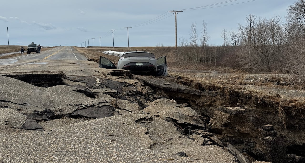 A car sunk on the side of a road where it's been washed out.