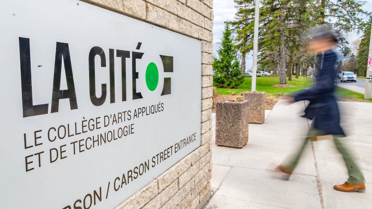 A woman walks past a sign for a francophone college.