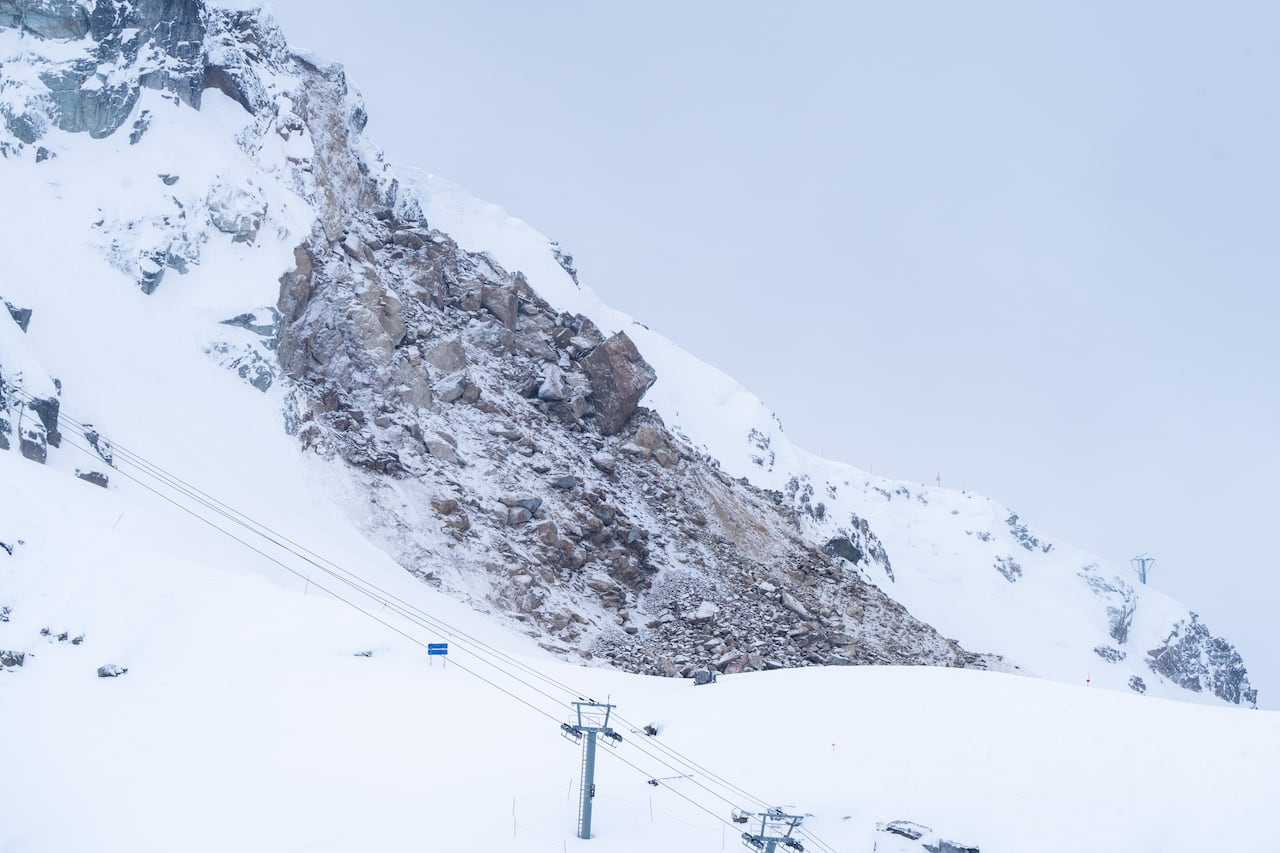 Massive brown rocks are seen along a slope on a snowy mountain in the daytime.