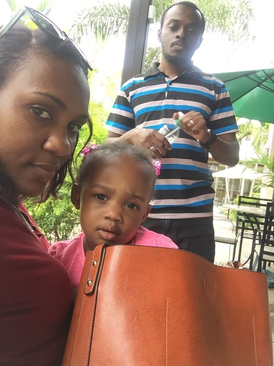 A woman sits next to a young child, a man behind them holding a water bottle as they all sit at an outdoor venue.