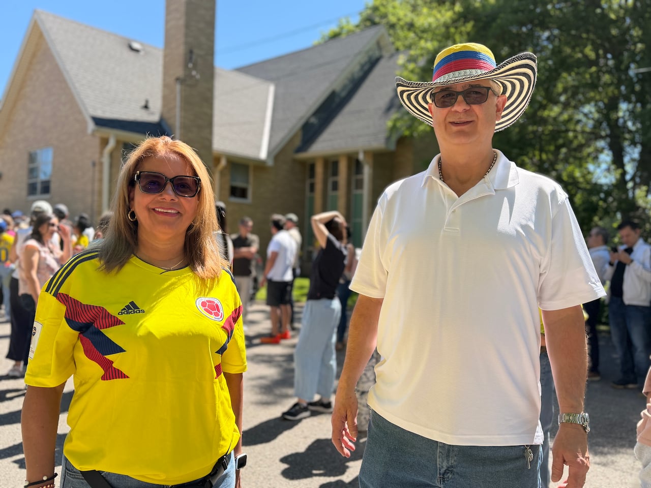 Two people smile at the camera. One wears a Colombia soccer jersey, the other wears a hat with the Colombian flag colours