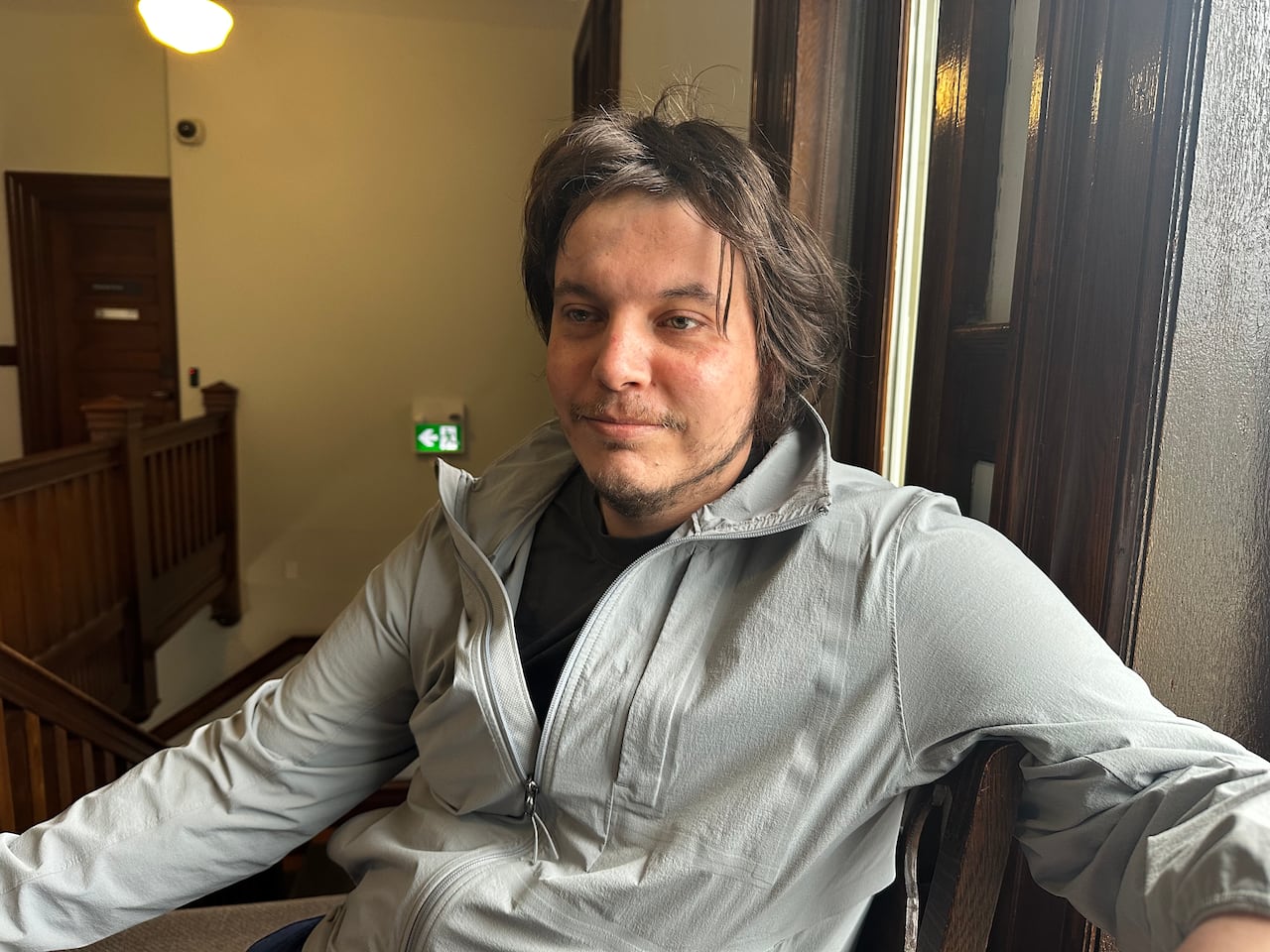 A man in a grey jacket is shown seated.
