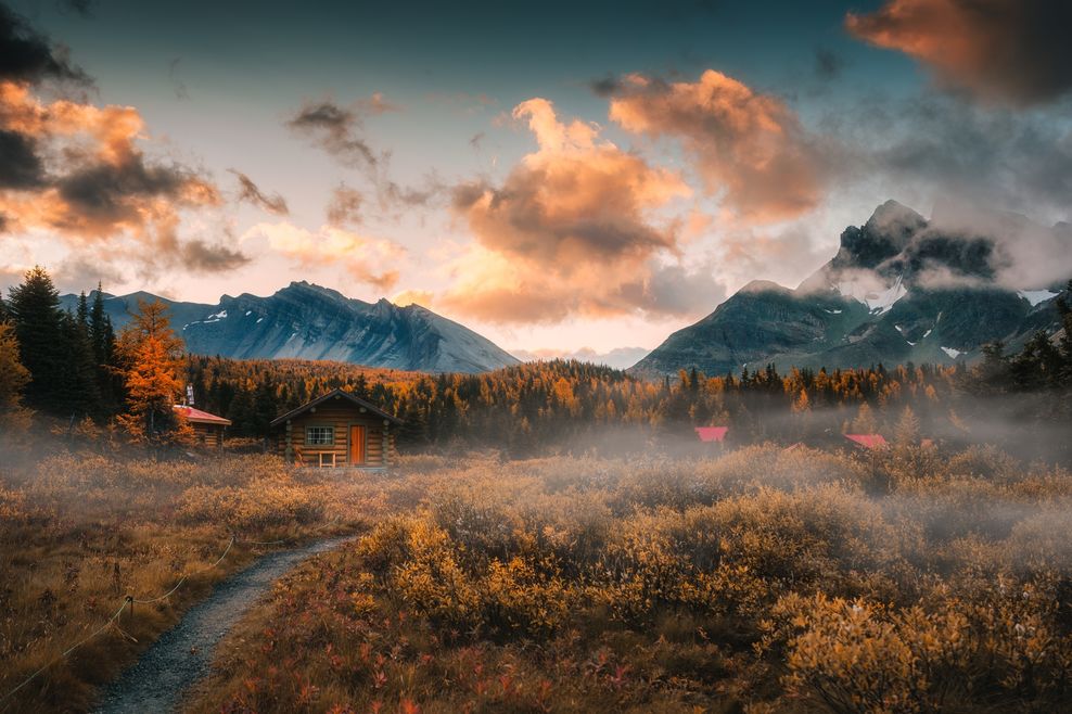 Scenic autumn landscape of wooden naiset huts with rocky mountains surrounded by golden autumn forest during morning in Assiniboine 
