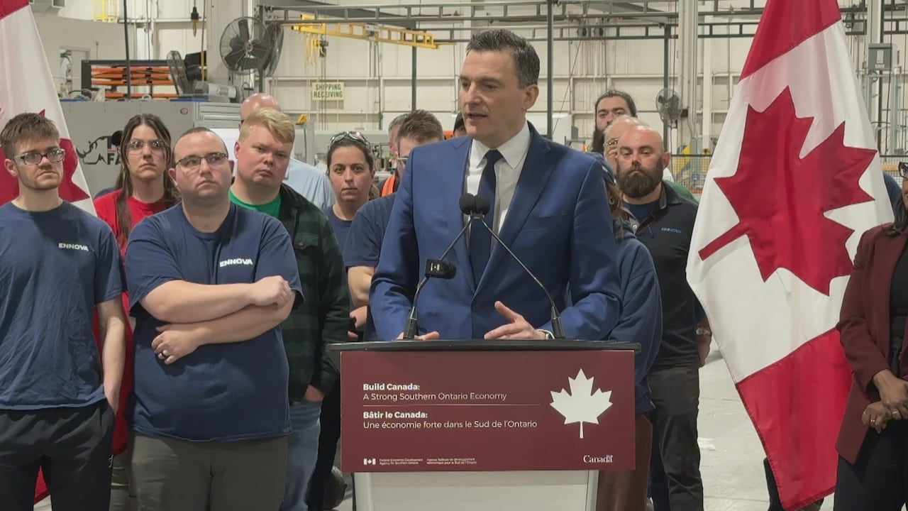 Solomon in a suit at a podium with a crowd of casually-dressed workers behind him.