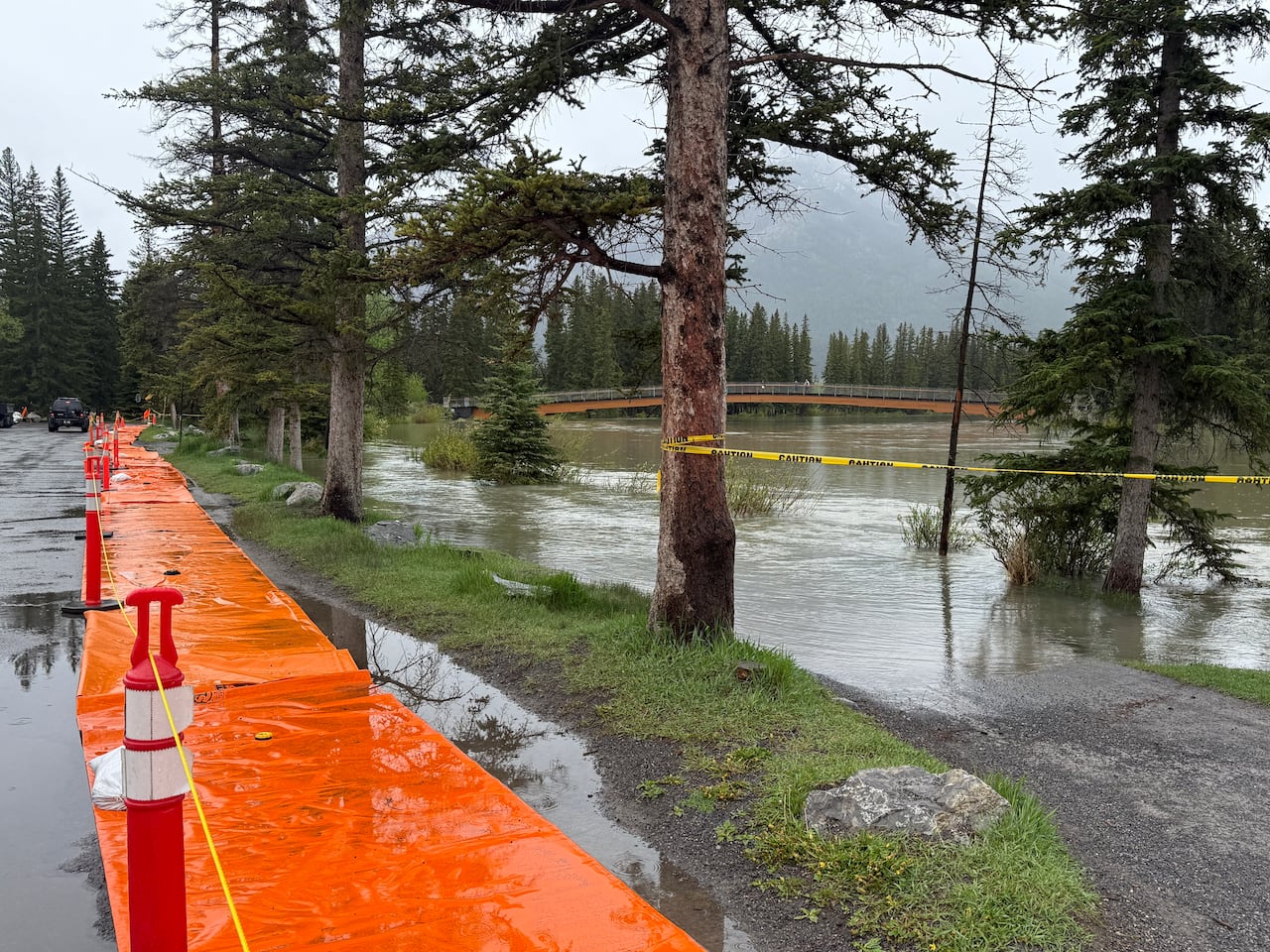 A river overflows onto a pathway. Bright orange berms line the adjacent road.