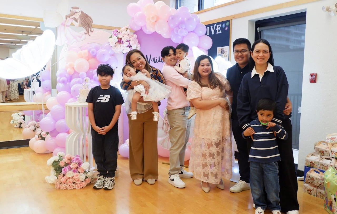 A group of people gather today for a photo, with pink and purple balloons in the background.
