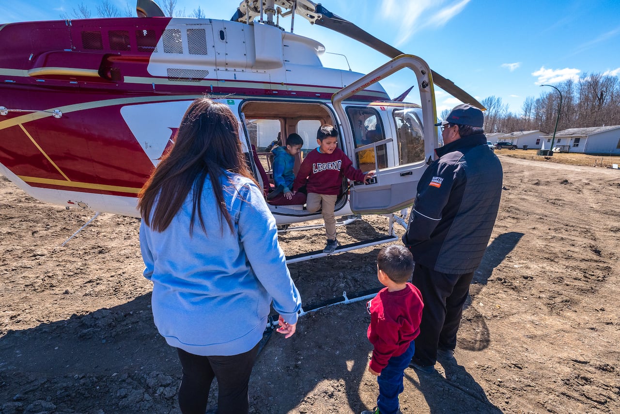 A man, woman and child wait outside a landed helicopter as two more children climb down from it.