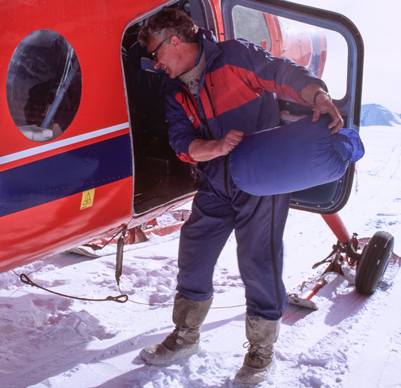 A man loads cargo onto a small plane in the snow.