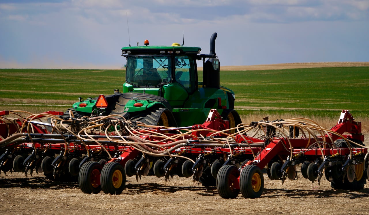 A green tractor and a red seeder are shown in a field.