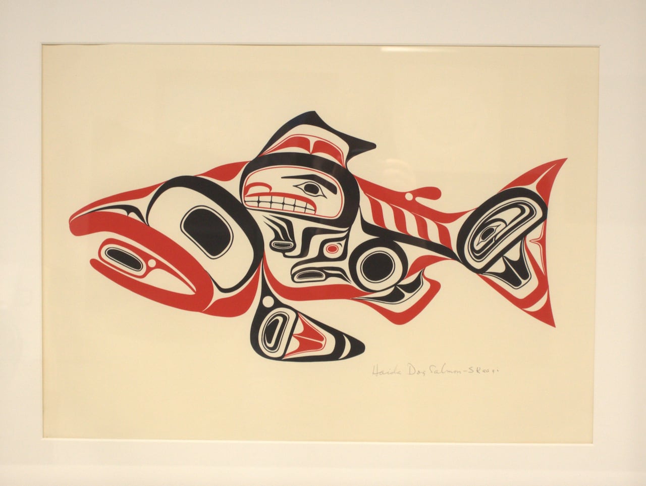 A framed print of a fish in the formline style using red and black lines and shapes.