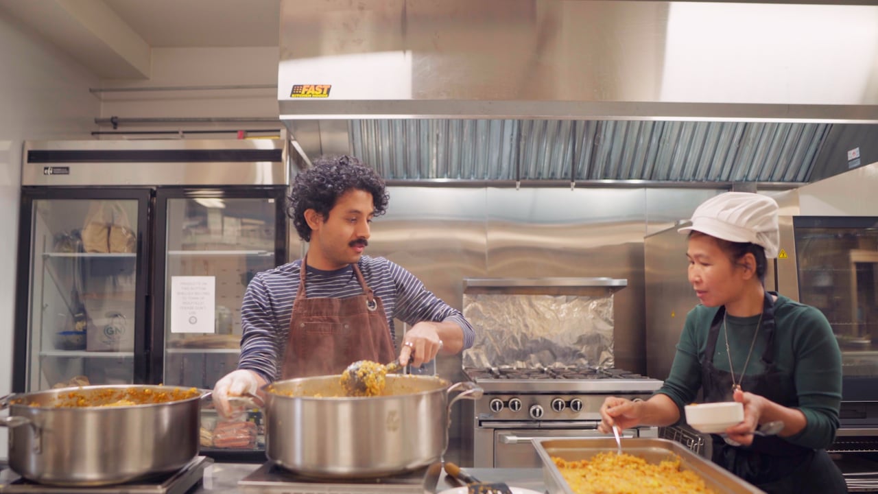 Two people are shown in a commercial kitchen prepping food.