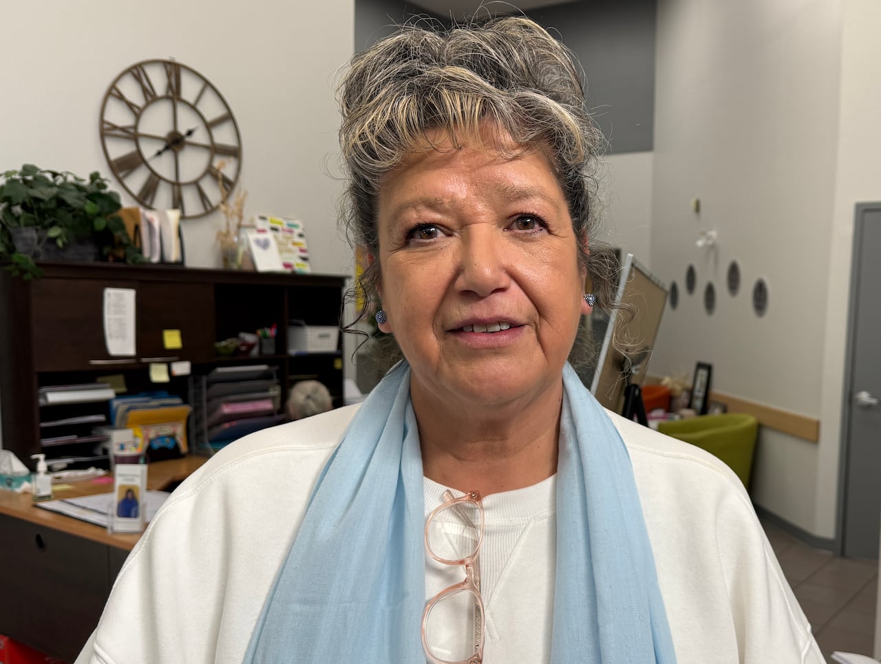 A woman in a white shirt and blue scarf stands in an office.