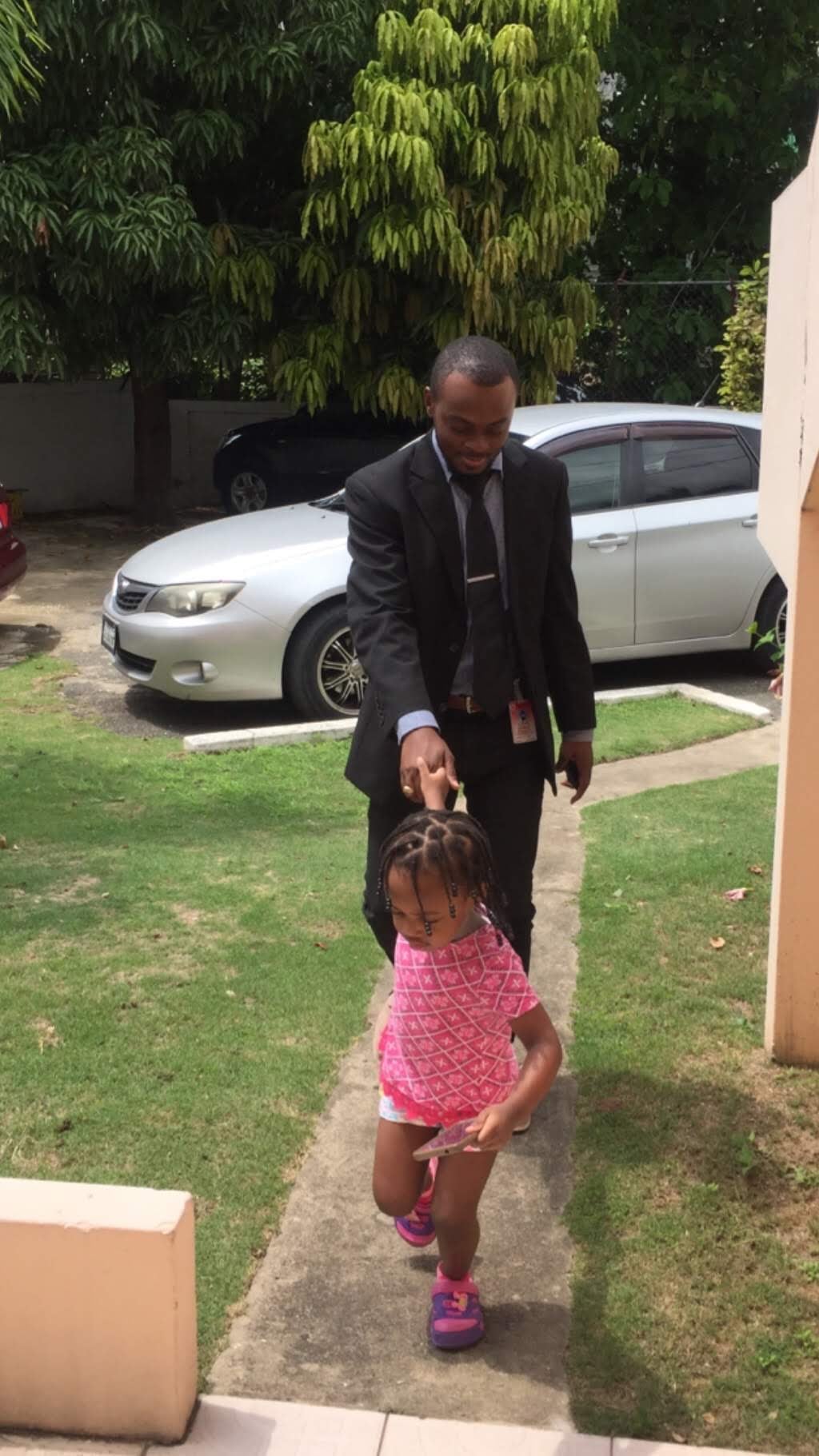 A man in a suit is led by hand by a child in a pink shirt walking up a path.