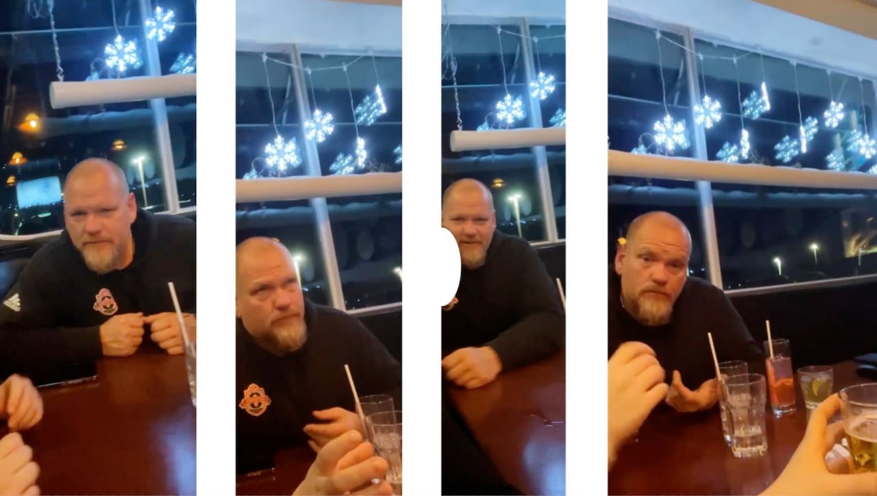 A man in a hooded black sweatshirt sitting at a table in a bar with drinks.