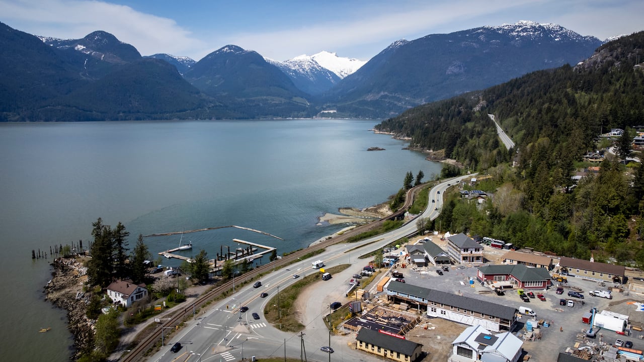 An aerial view shows a coastal highway, railway tracks, and a small town.