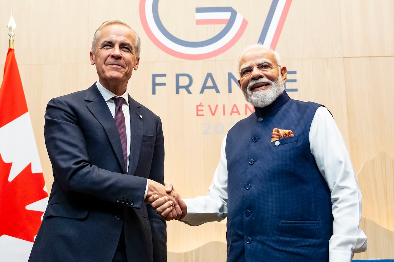 Carney and Modi shake hands in front of a G7 sign as they smile to the camera.