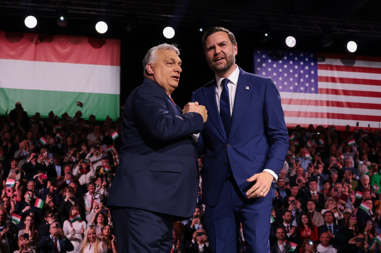 Two men in suits shake hands in front of a crowd.