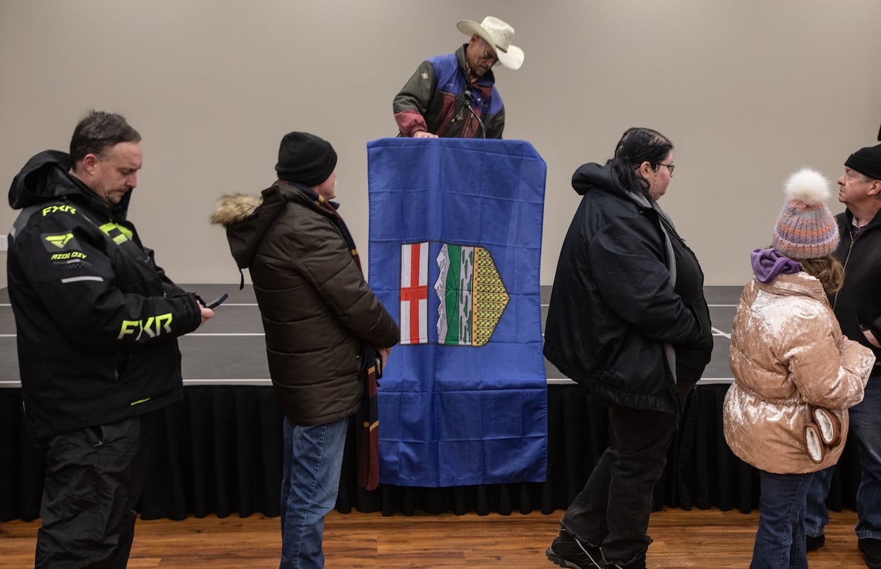 People line up in front of an Alberta flag.
