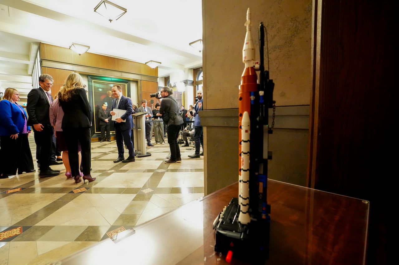 A Lego model of an Artemis rocket sits on a desk with people in the background