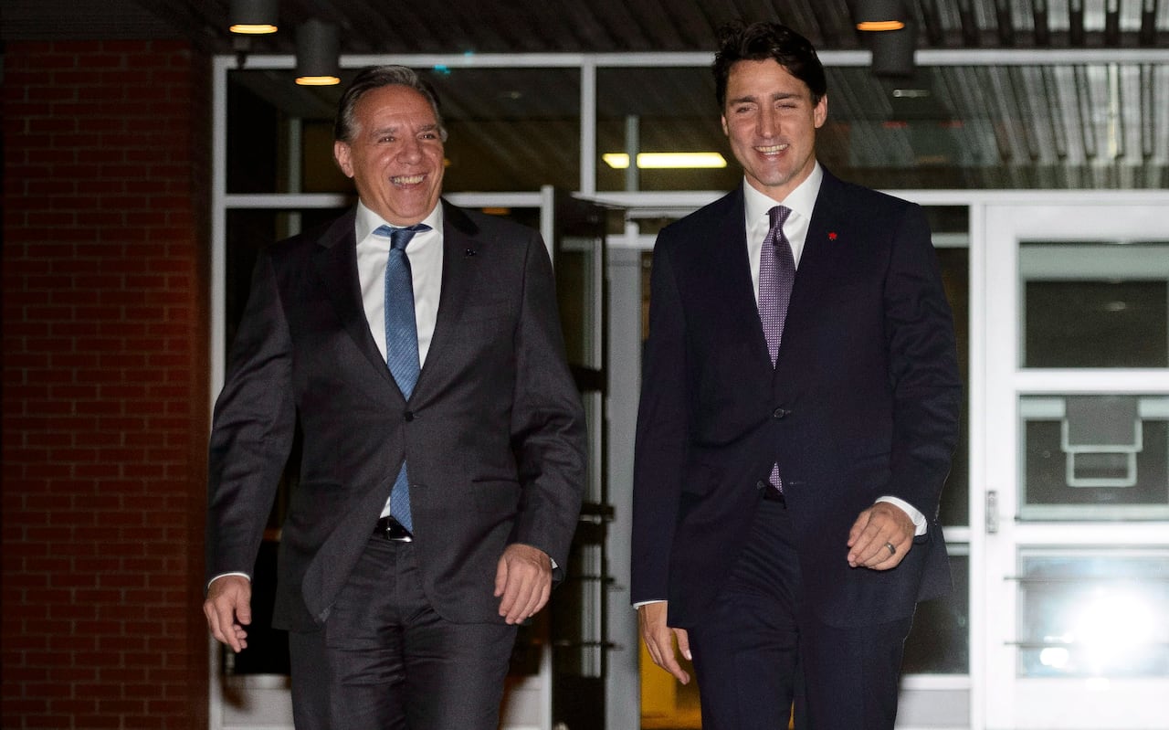 Two men in suits walk out of a building smiling.