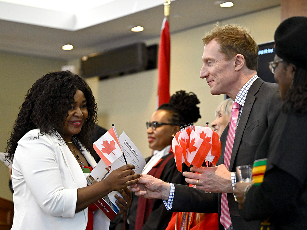 A new Canadian recieves a Canadian flag from the Citizenship minister