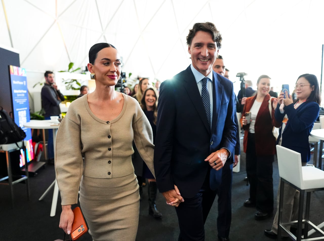 A man and woman hold hands while walking through a crowd.