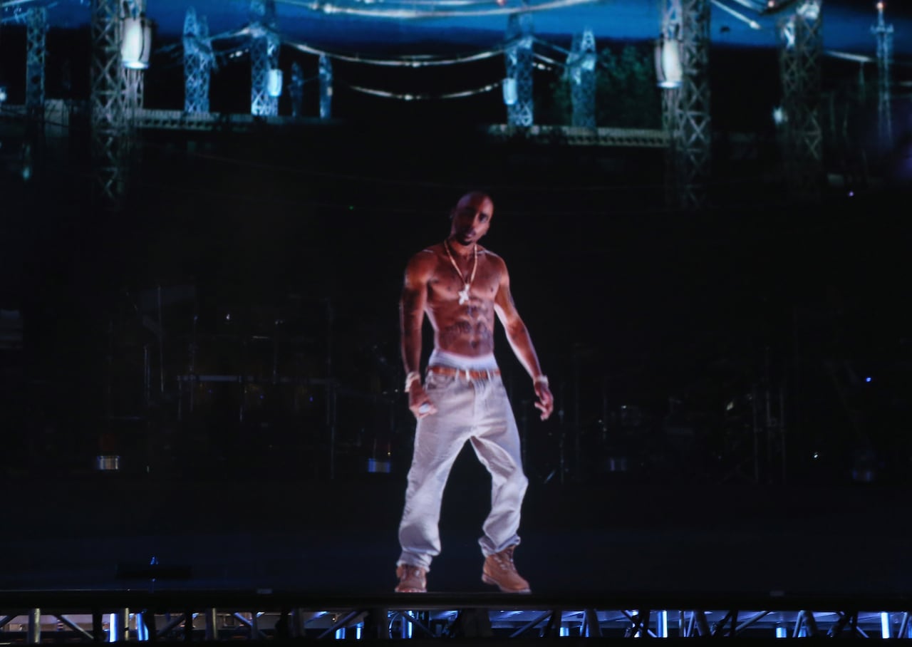 A digital projection of a shirtless Black man is seen on a large concert stage.