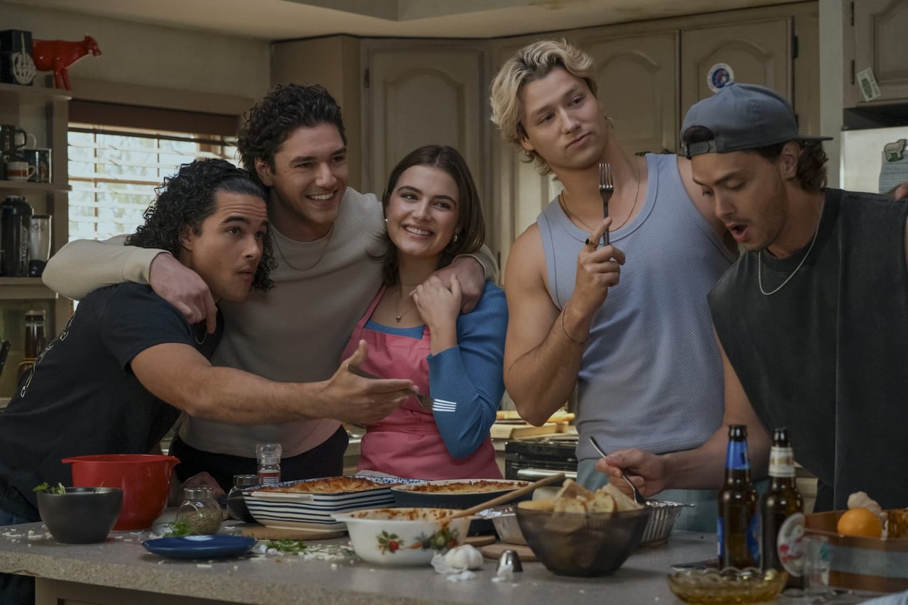 Four college-aged men and one woman in the kitchen hanging out.