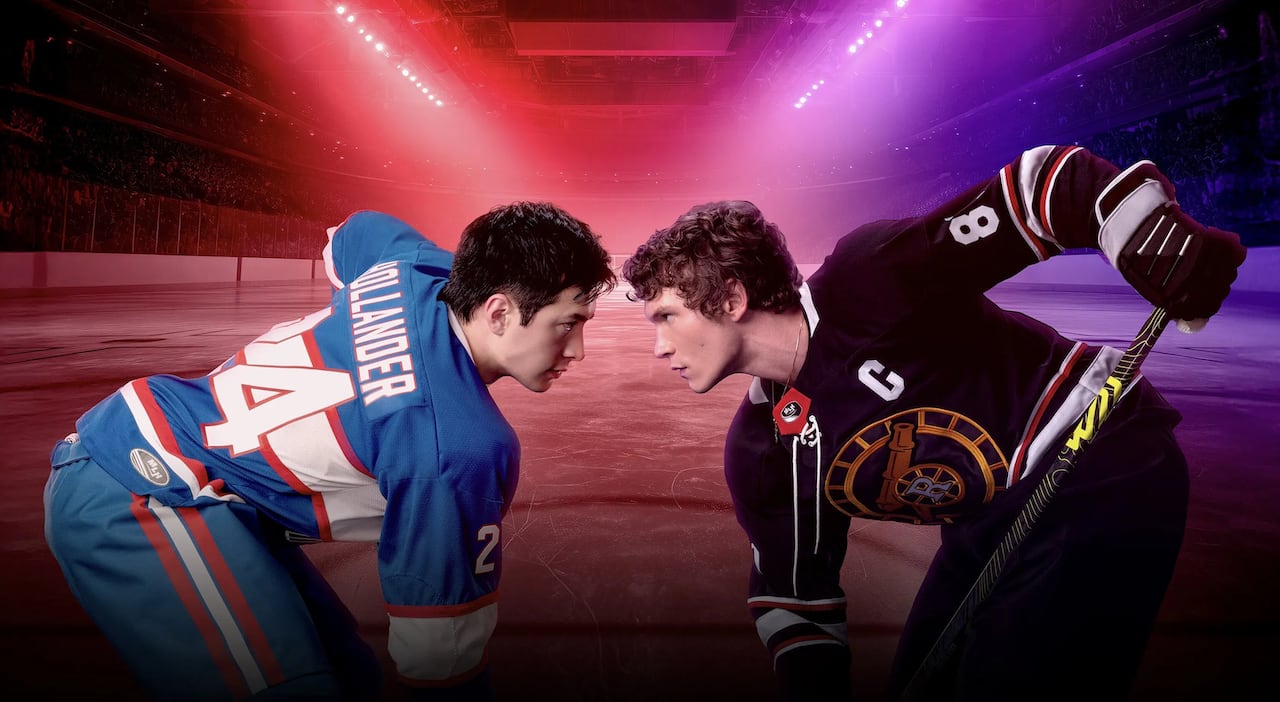 Man with short hair on the left in a hockey jersey faces off against man with curly hair on the right in a hockey jersey. They have hockey sticks on the ice.