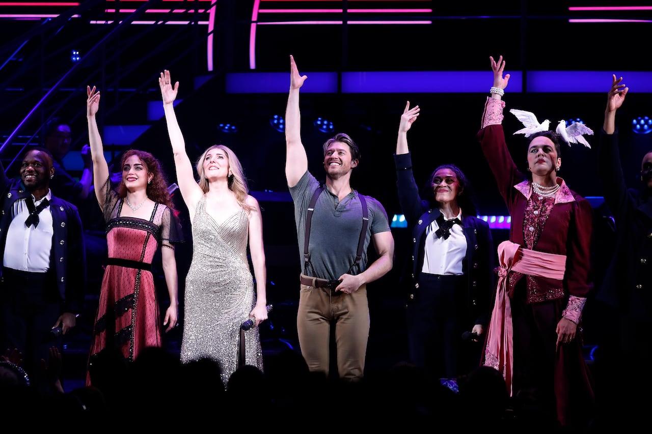 Six people, raising their right arms in the air in a dark space.