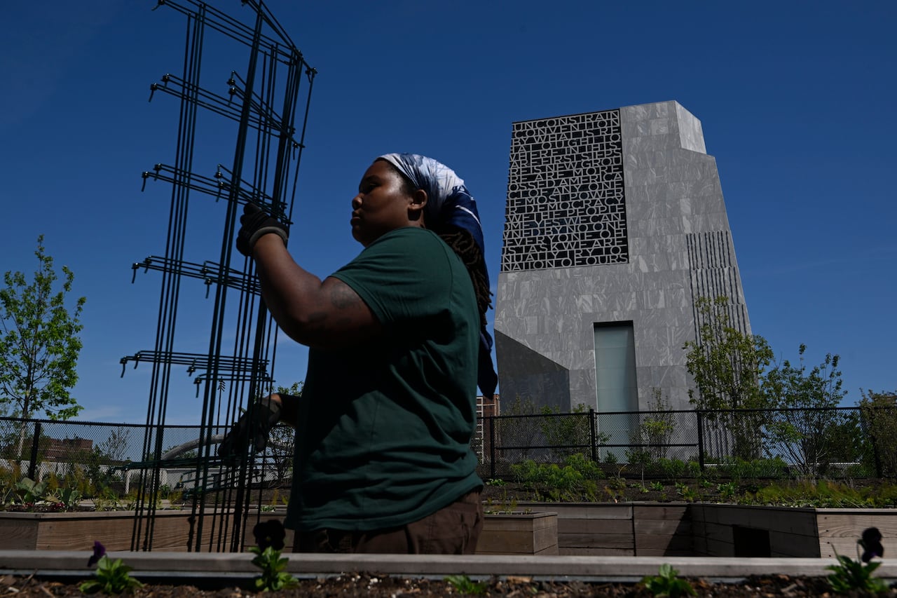 A labourer carries construction equipment. Behind them is a large, imposing concrete building.