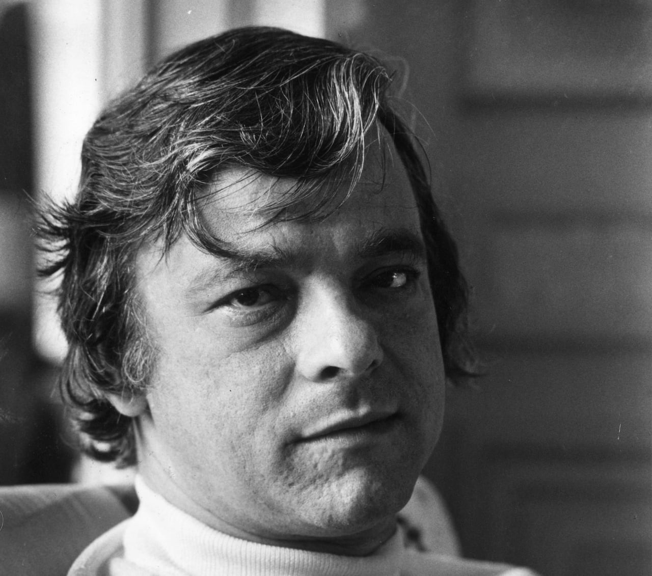 A man with curly hair, body facing the right, while facing the front.