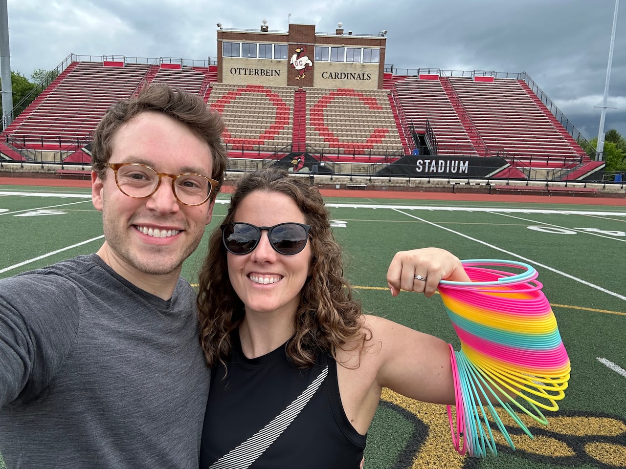A man and a woman pose for a photo, the woman flexes with a slinky toy on her arm