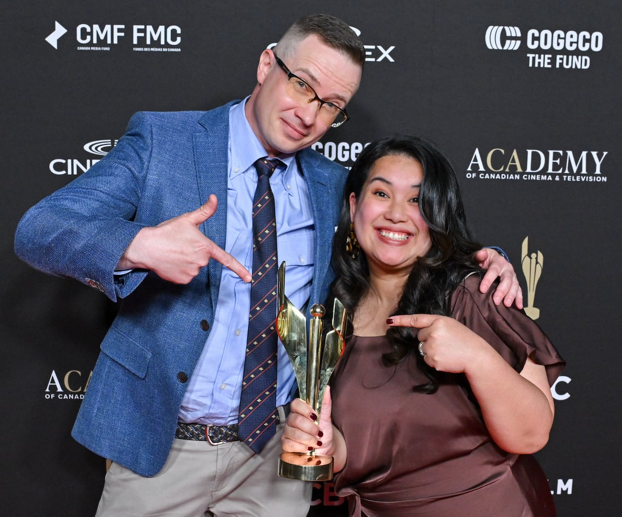 Man in suit poses with woman in brown dress holding award.
