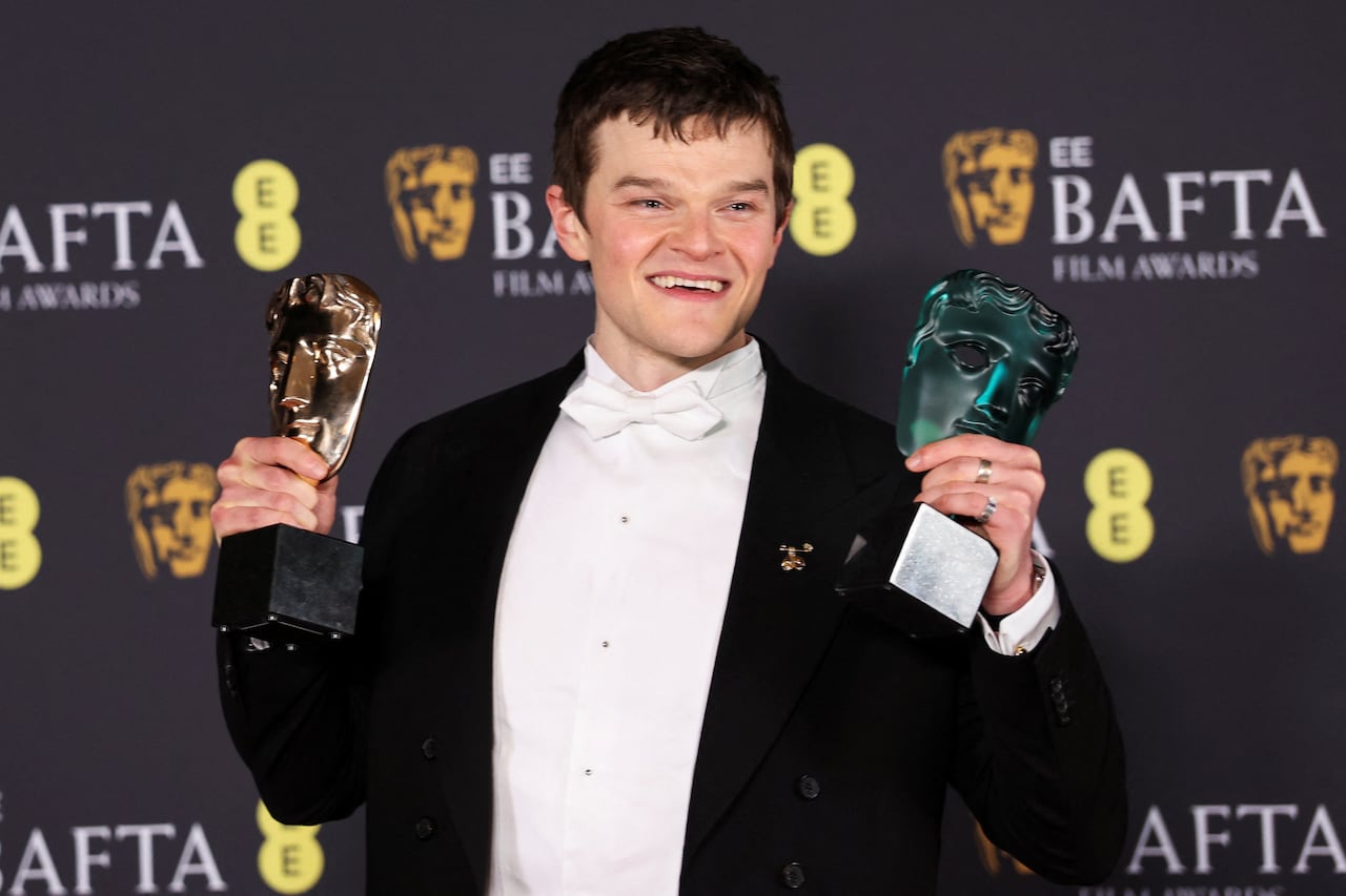 A man in a tuxedo holds an award in each hand
