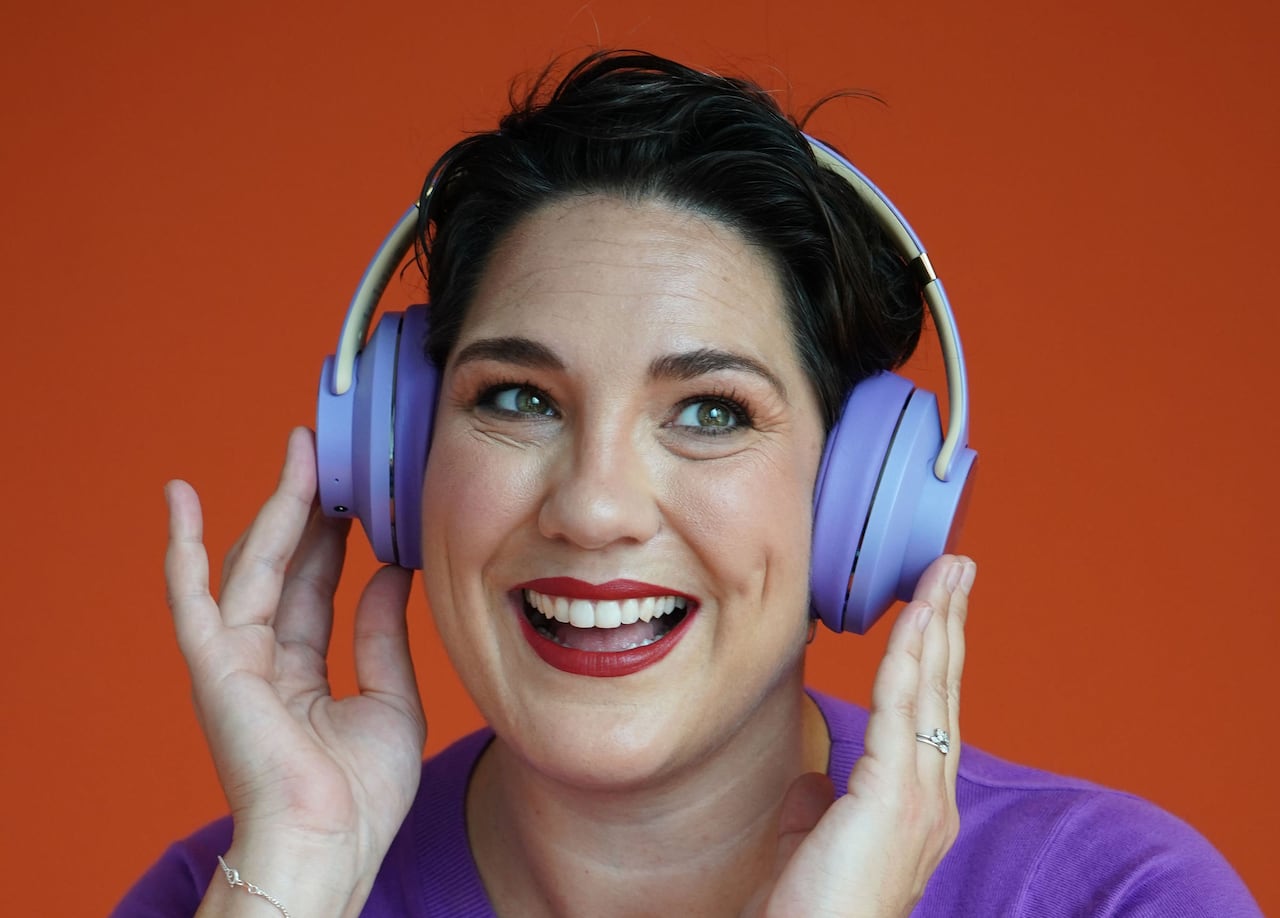 Woman wearing bluish purple headphones, smiling.