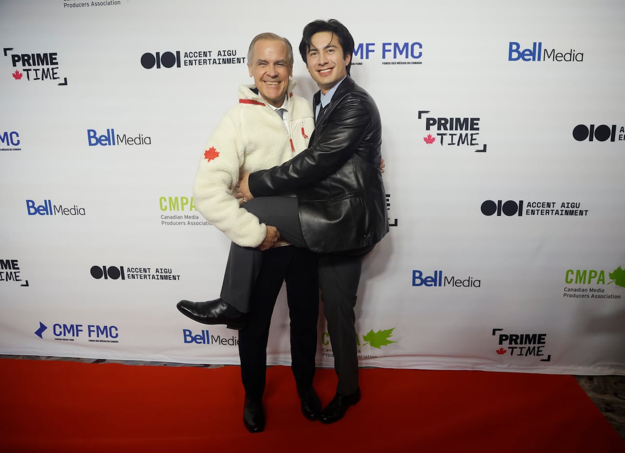 A man in a white fleece holds up the leg of another man as they smile for a photo.