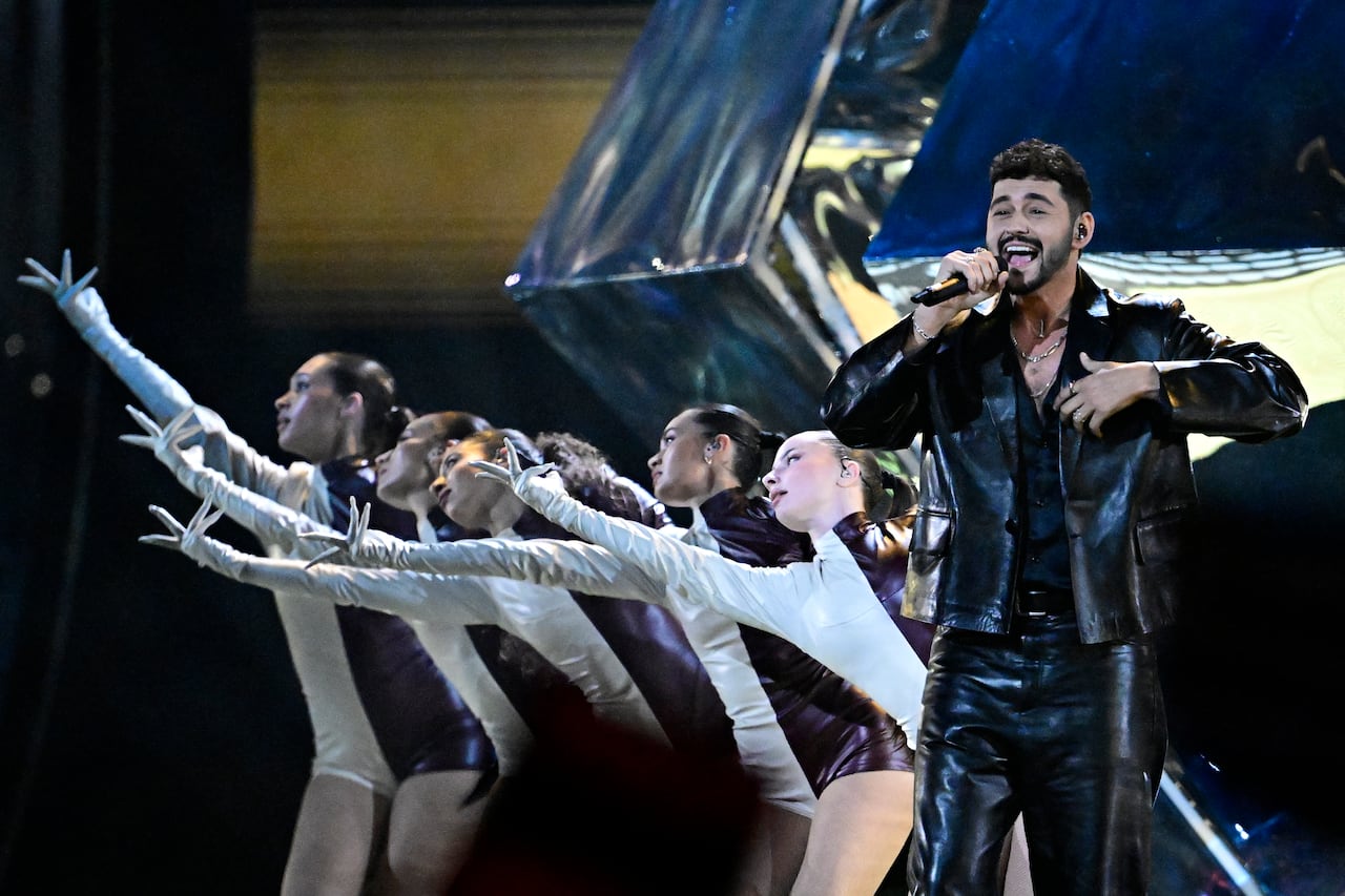 Singer in black with dancers with arms outstretched to his left.