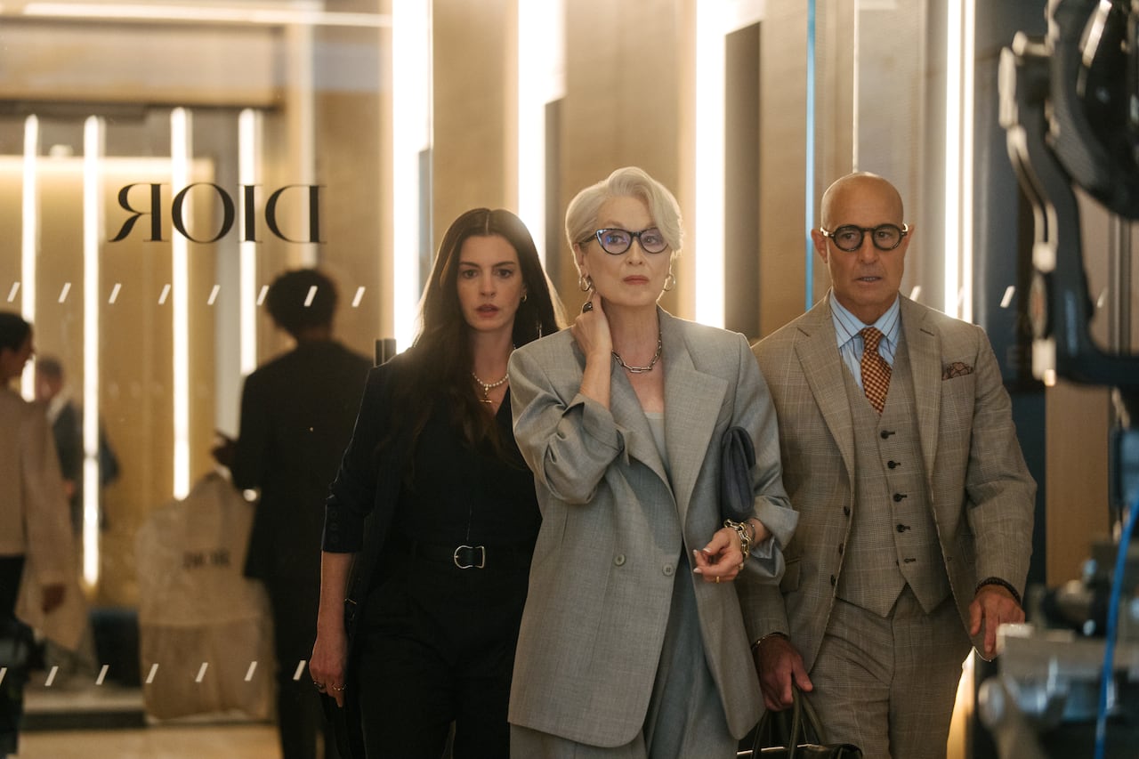 Three people wearing fine clothes walk away from a glass door.