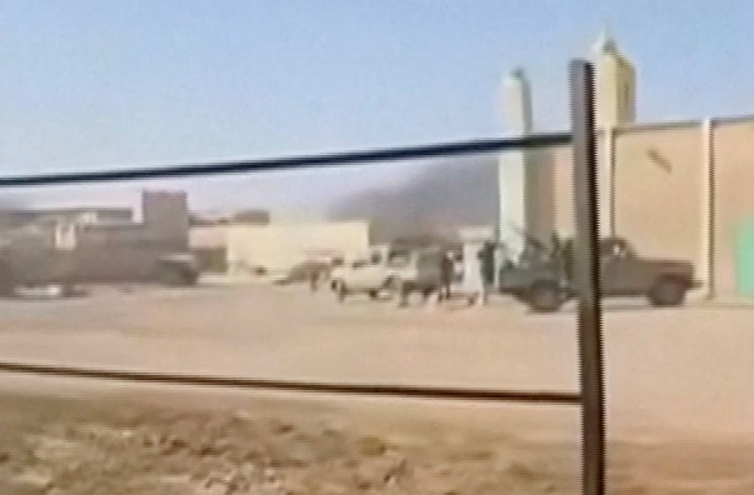 Smoke rises behind an industrial and sandy looking parking lot.
