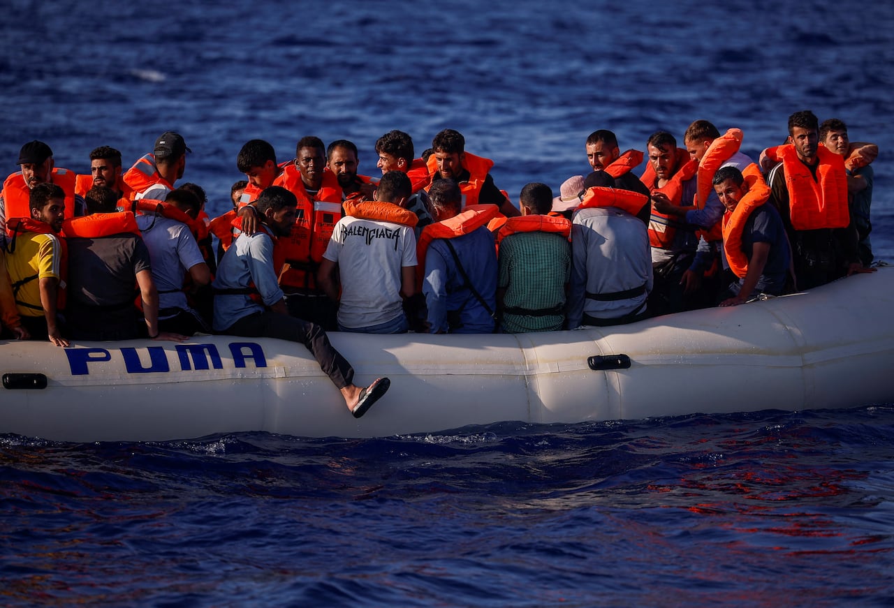 Dozens of people with life preservers are shown on a rubber boat.