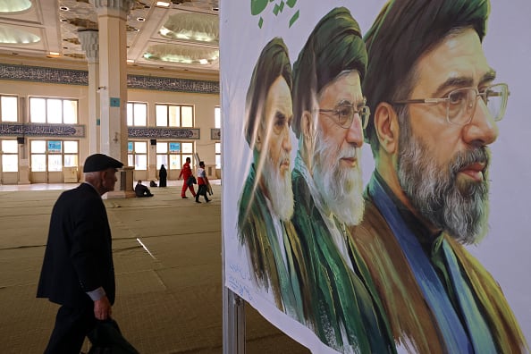An older man walks past an image of three Iranian supreme leaders.