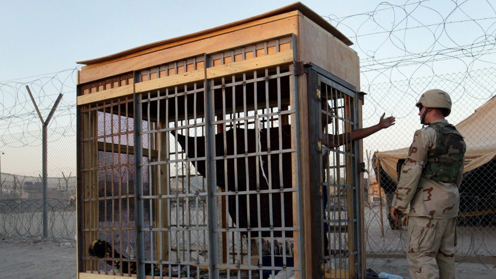 A detainee in an outdoor solitary confinement cell talks with a military policeman at the Abu Ghraib prison on the outskirts of Baghdad, Iraq in this June 22, 2004 photo. (AP Photo/John Moore)
