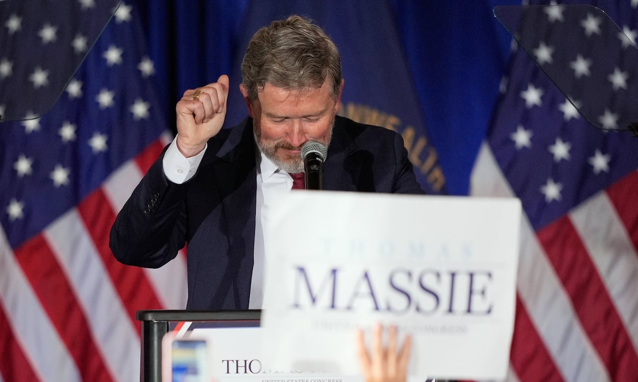 Thomas Massie holds his clenched right fist in the air, as someone's hand in the foreground holds up a sign that reads 'Massie'