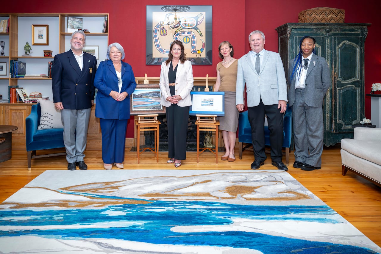Several people stand beside a large rug.