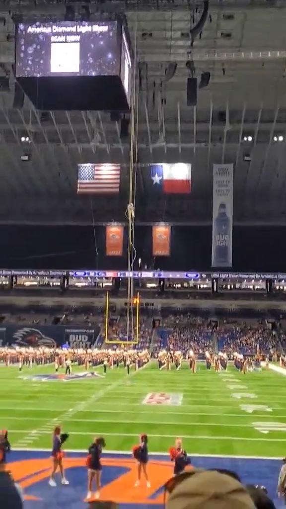 A military member falls from a rope high above a football field during a pregame stunt in a stadium.