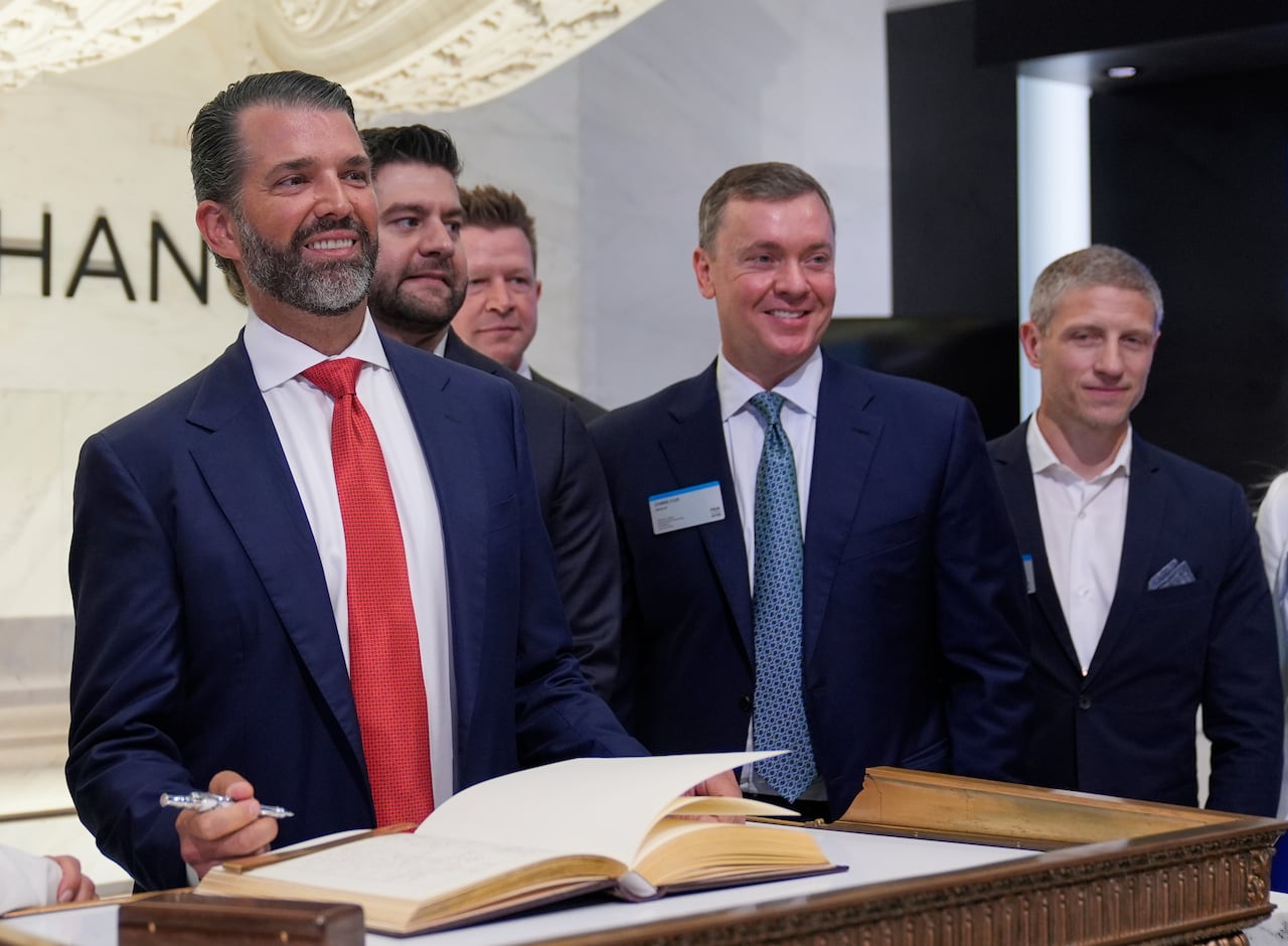 Five men pose for a photo, one of them is holding a pen in his hand over a book.